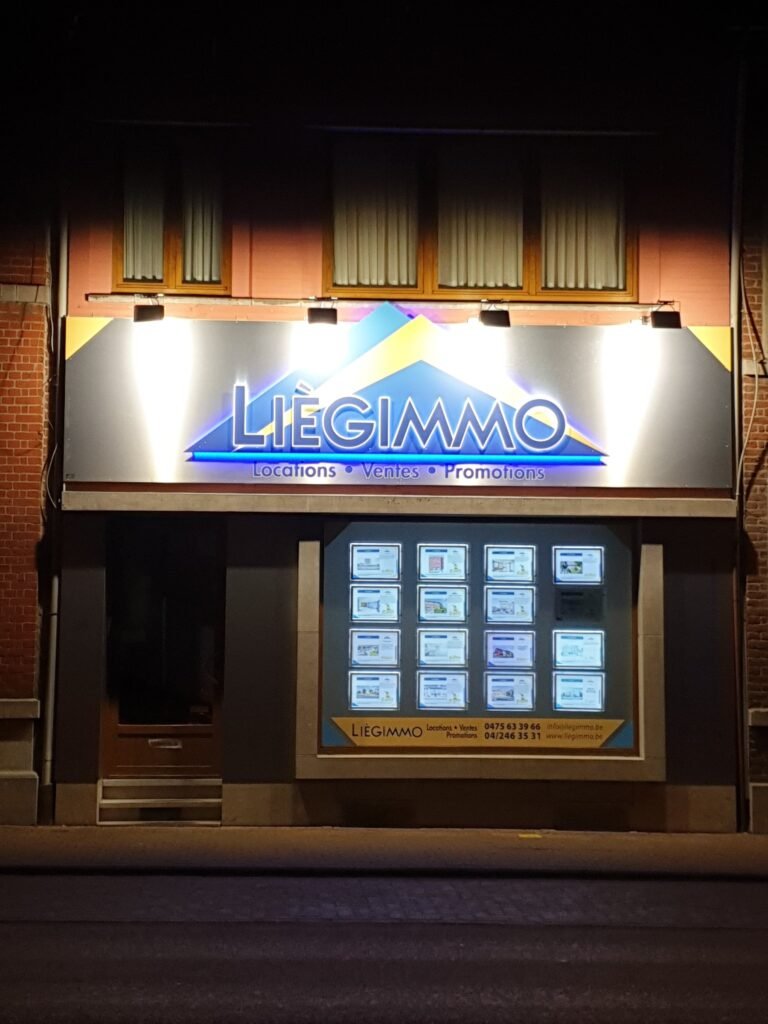 Enseigne de l’agence LiègeImmo, éclairée, de nuit
